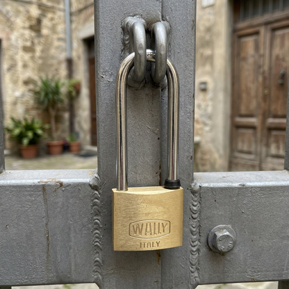 Lucchetto in ottone Wally 275EL con arco extra lungo inserito negli occhielli di un cancello in metallo grigio

